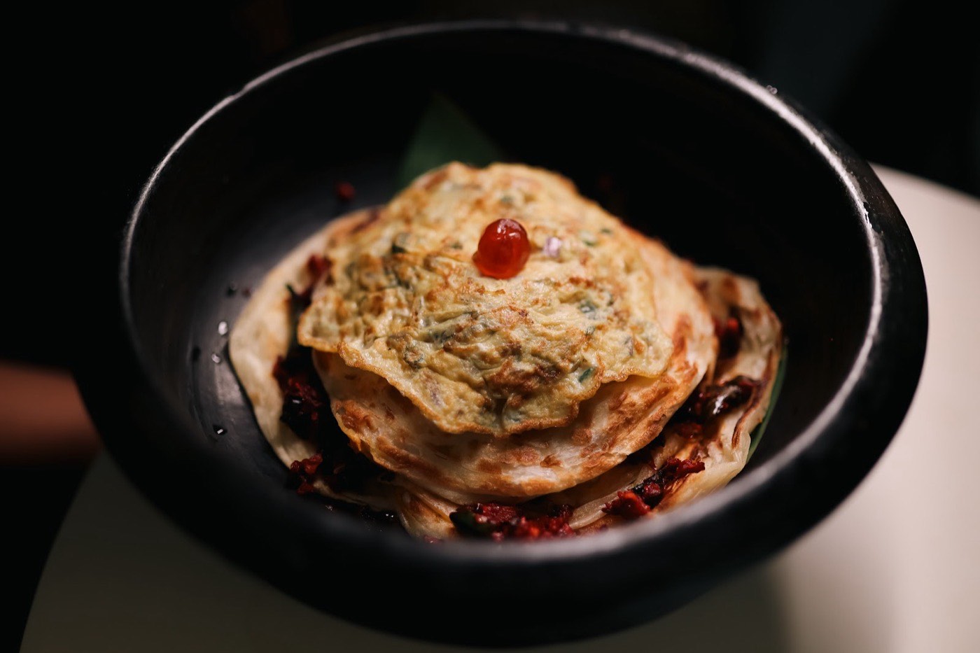 Layered Malabar egg porotta stacked in a black claypot at Chai Kadai